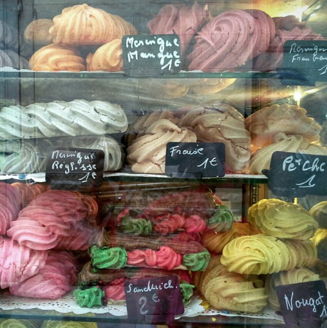 A display case filled with colorful meringue pastries, labeled with prices and flavors such as mango, strawberry, and nougat.